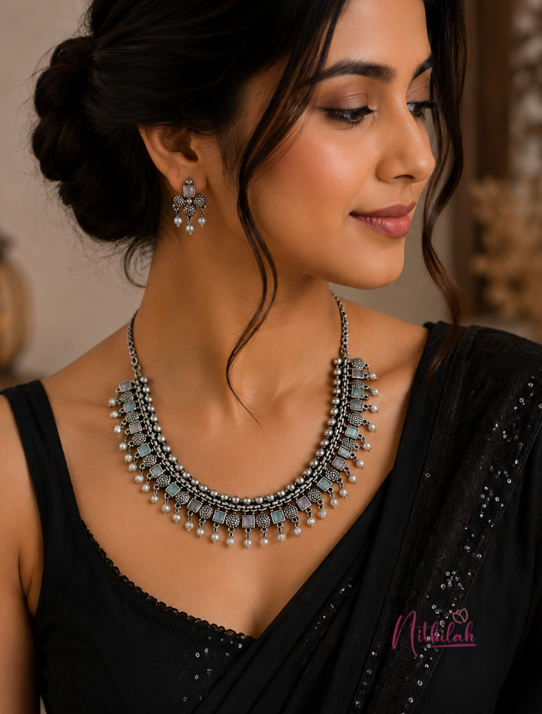 South Indian woman wearing a premium oxidised silver necklace set with pastel mint and pastel pink stones and matching earrings.