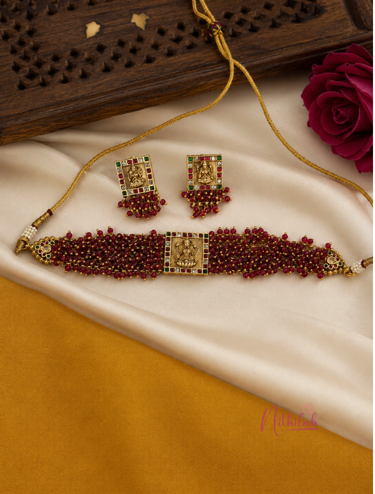 Antique Gold Lakshmi Temple Choker Necklace Set with ruby-red beads and matching Temple earrings displayed on silk fabric.