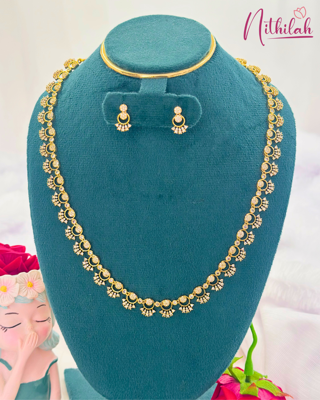 Gold-finish CZ floral necklace and matching earrings displayed on a teal jewellery bust