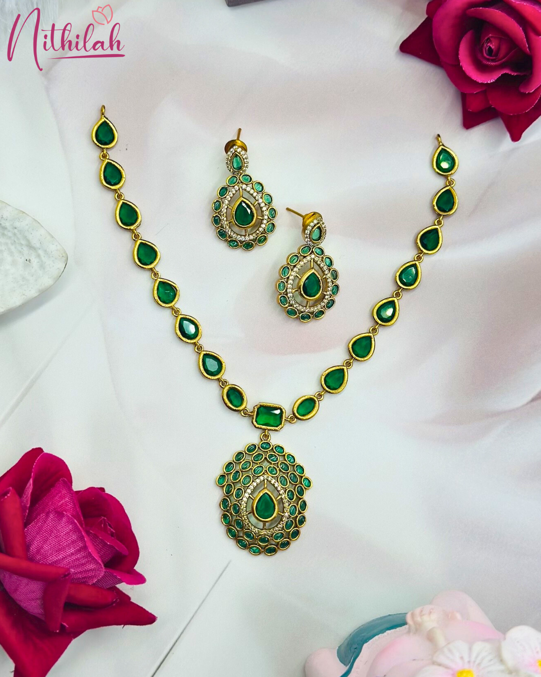 Emerald-green necklace set laid flat, showing teardrop stone links, an oval-bordered pendant and matching drop earrings