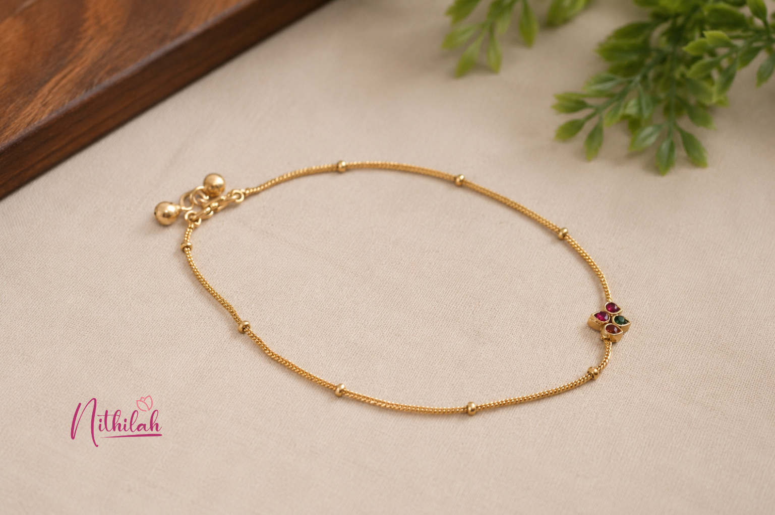 Close-up of an Antique Gold Finish Floral Chain Anklet with red and green stones under natural lighting.