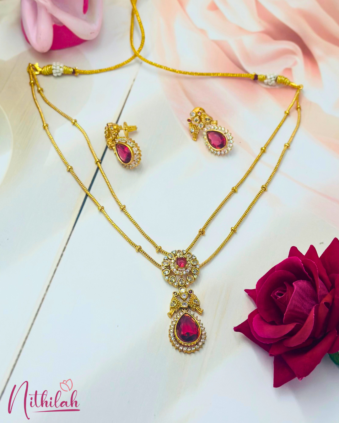 Gold-finish double-layer necklace with a ruby-pink teardrop pendant, clear stone detailing and matching earrings