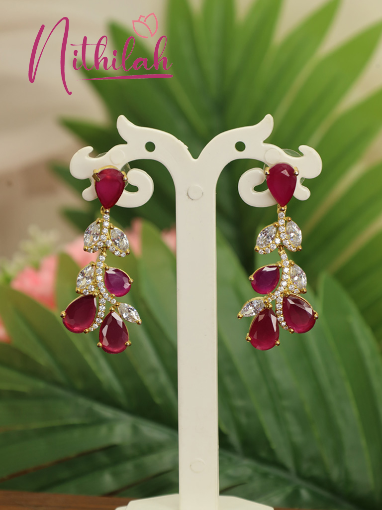 Pair of gold-plated ruby red American Diamond floral drop earrings featuring teardrop stones and sparkling leaf-shaped accents displayed on a jewellery stand.