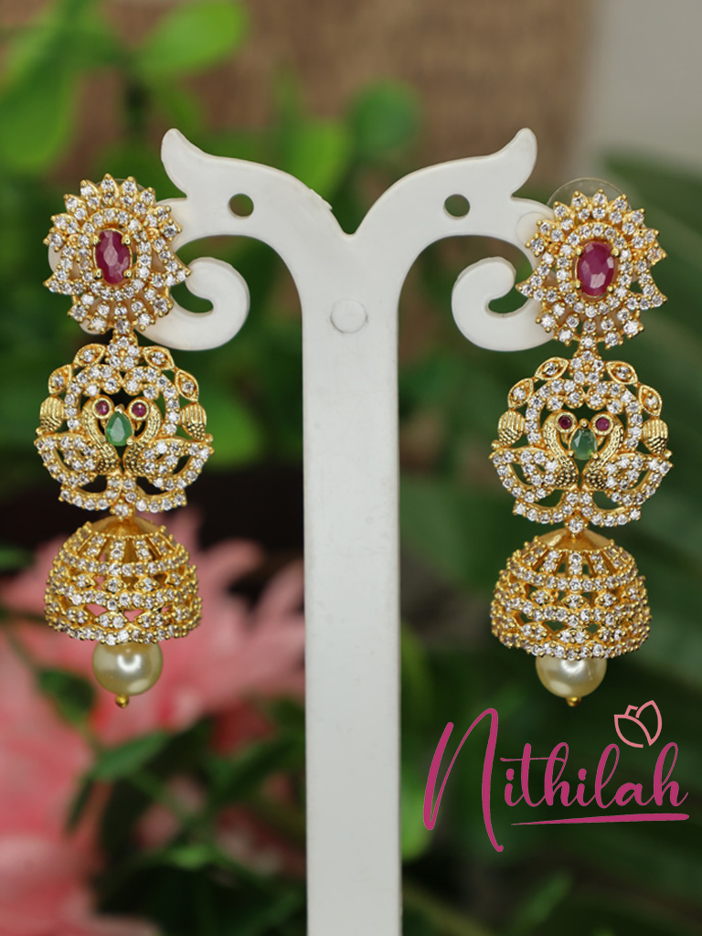 Gold-polished peacock stone jhumka earrings with pearl-like drops on a white display stand