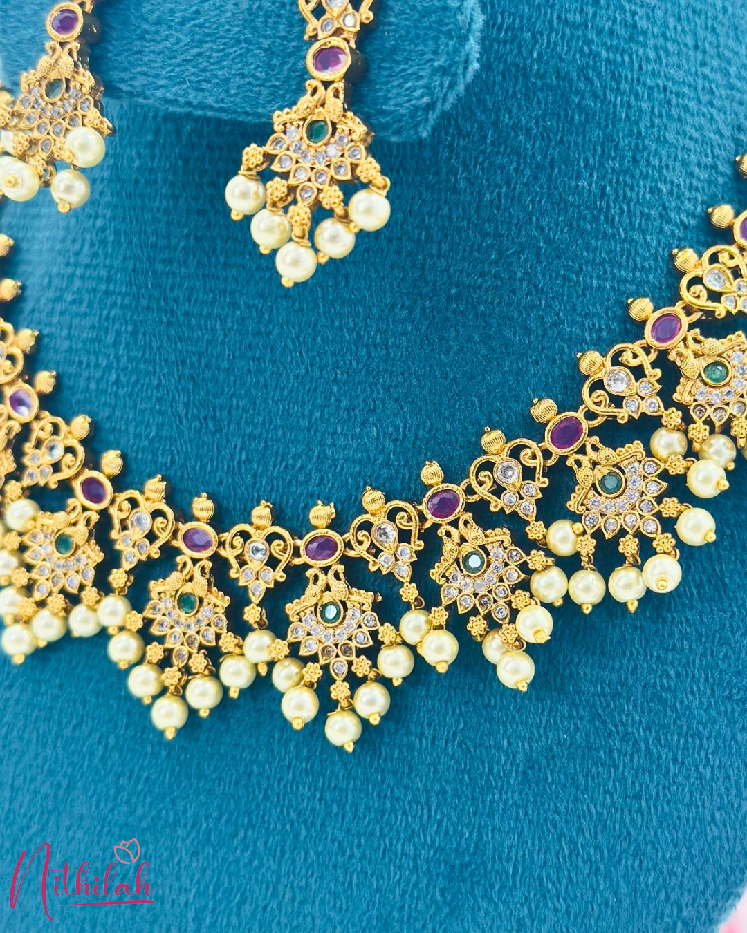 Close-up of gold-tone necklace detailing with clear floral stones, purple oval stones, green centres and pearl drops
