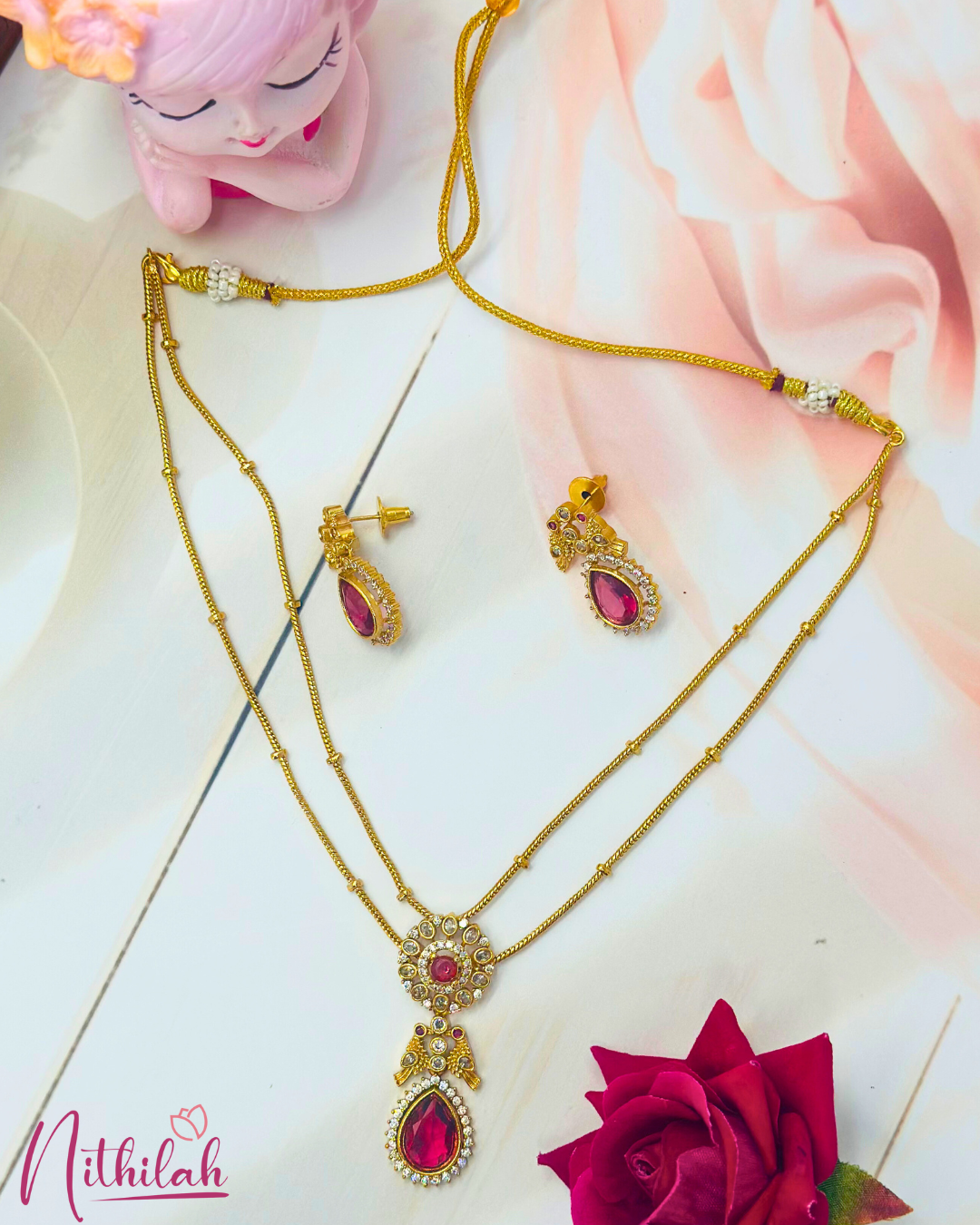 Ruby-pink teardrop necklace set laid flat, showing double-layer gold-finish chains, matching earrings and adjustable thread