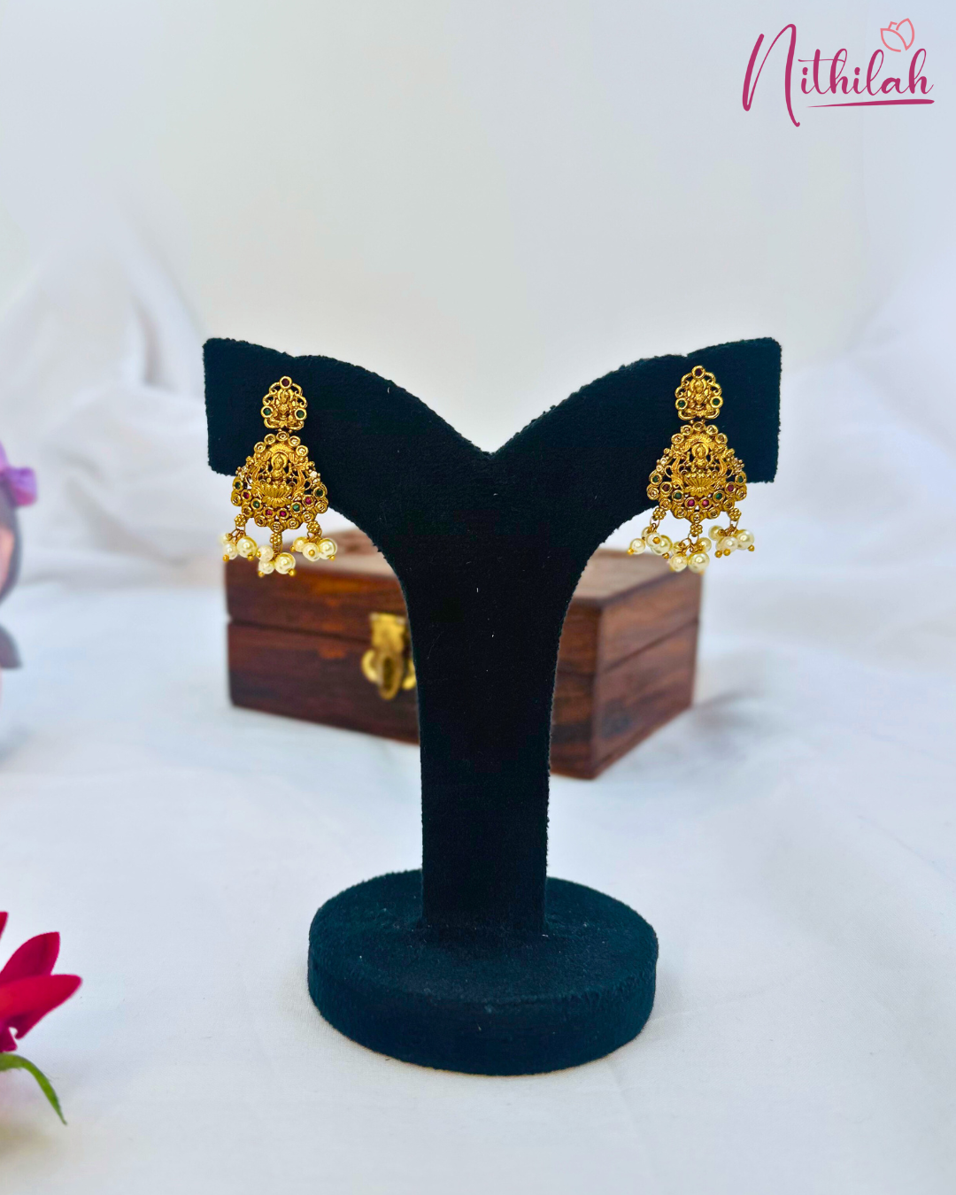 Antique gold-tone Lakshmi drop earrings with ornate detailing and white pearl fringes on a black earring stand
