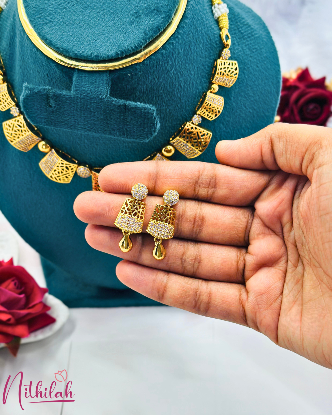 Close-up of gold-plated latticework earrings with CZ bands and polished teardrop drops, held in a hand