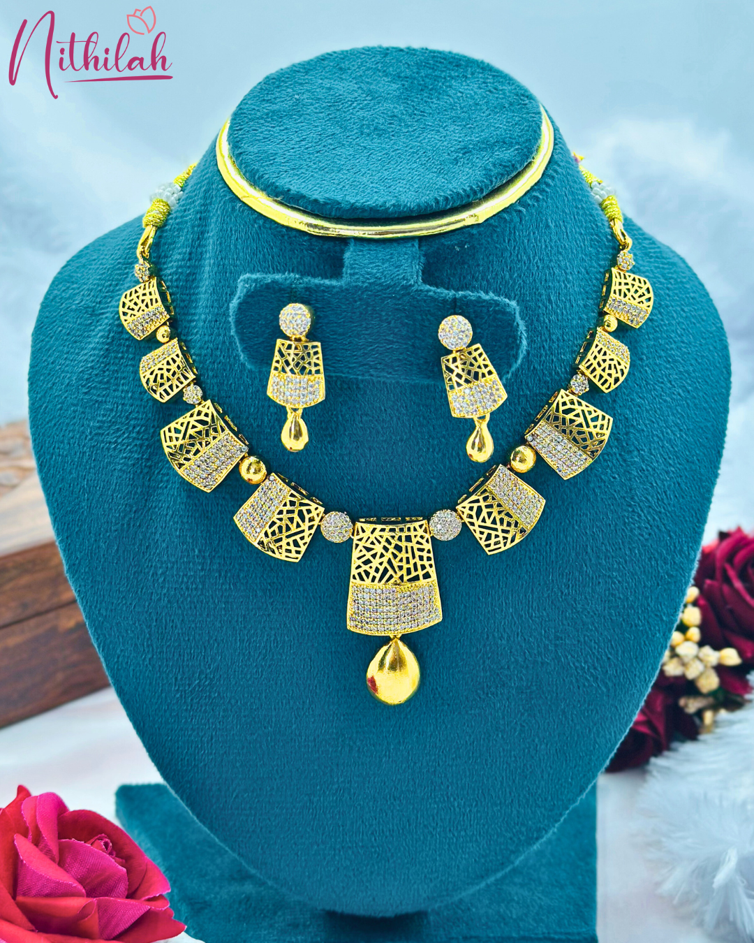 Gold-plated geometric CZ necklace set with latticework panels and matching drop earrings on a teal display bust