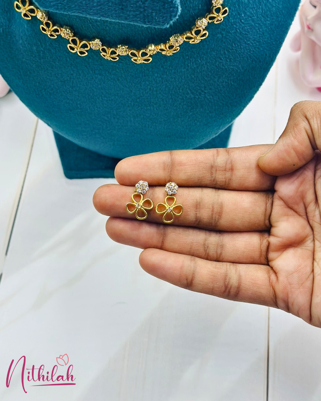 Close-up of gold-finish four-petal flower earrings with round CZ stone clusters, held in a hand