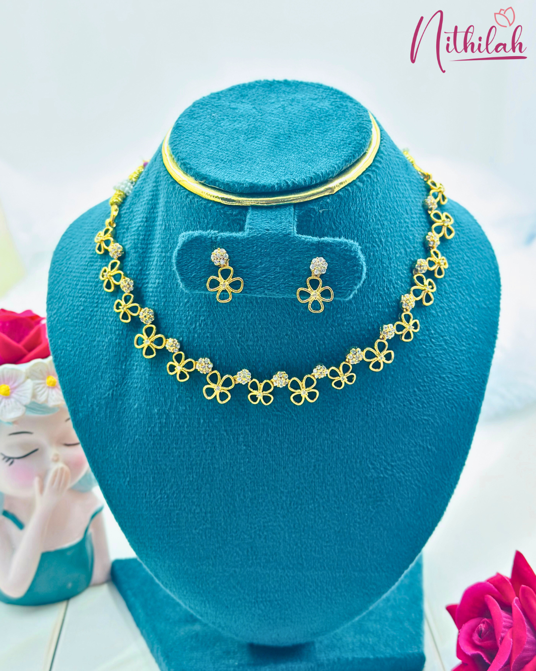 Gold-finish flower CZ necklace and matching floral earrings on a teal display bust
