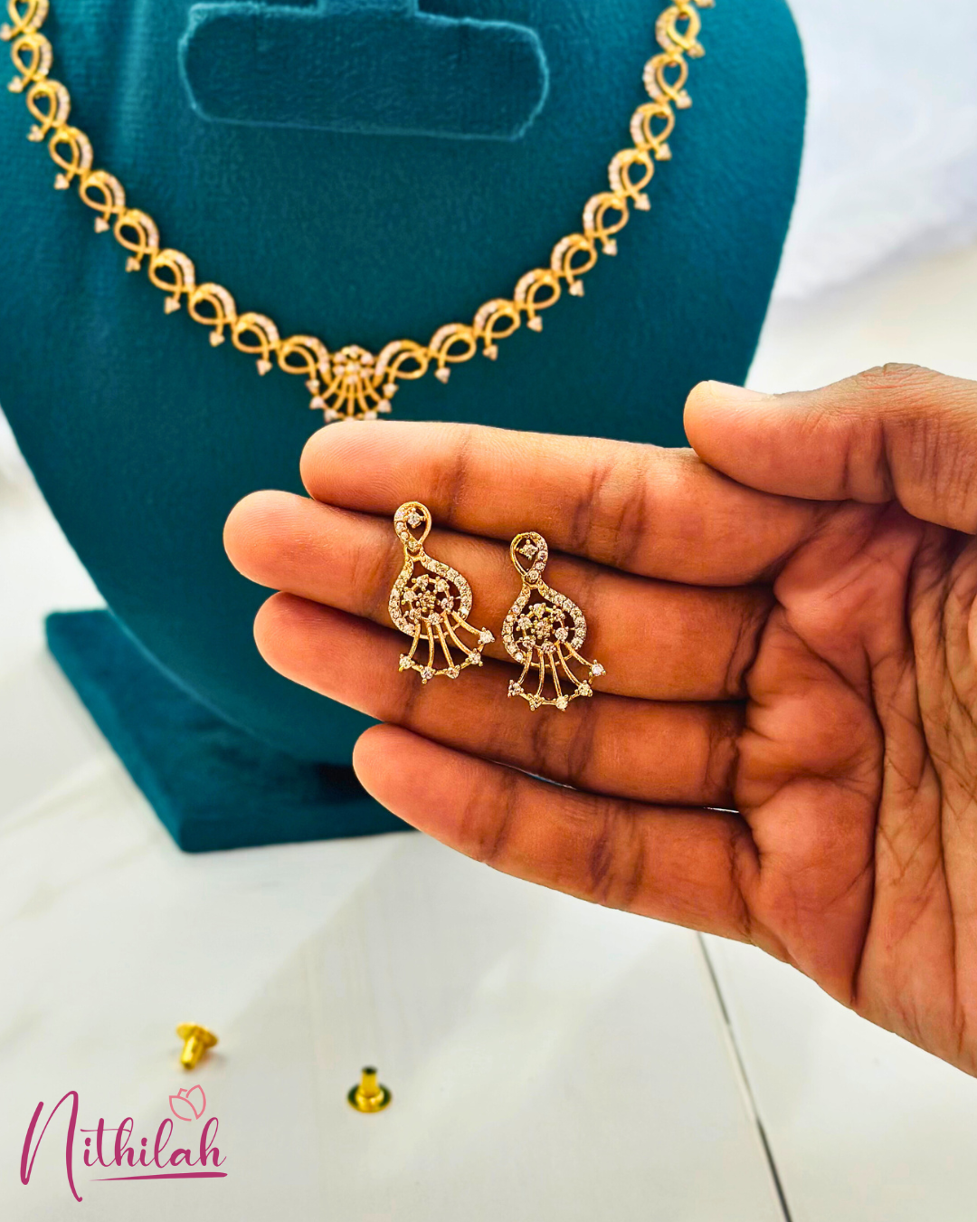 Close-up of gold-plated CZ drop earrings with paisley curves and fan-shaped detailing, held in a hand