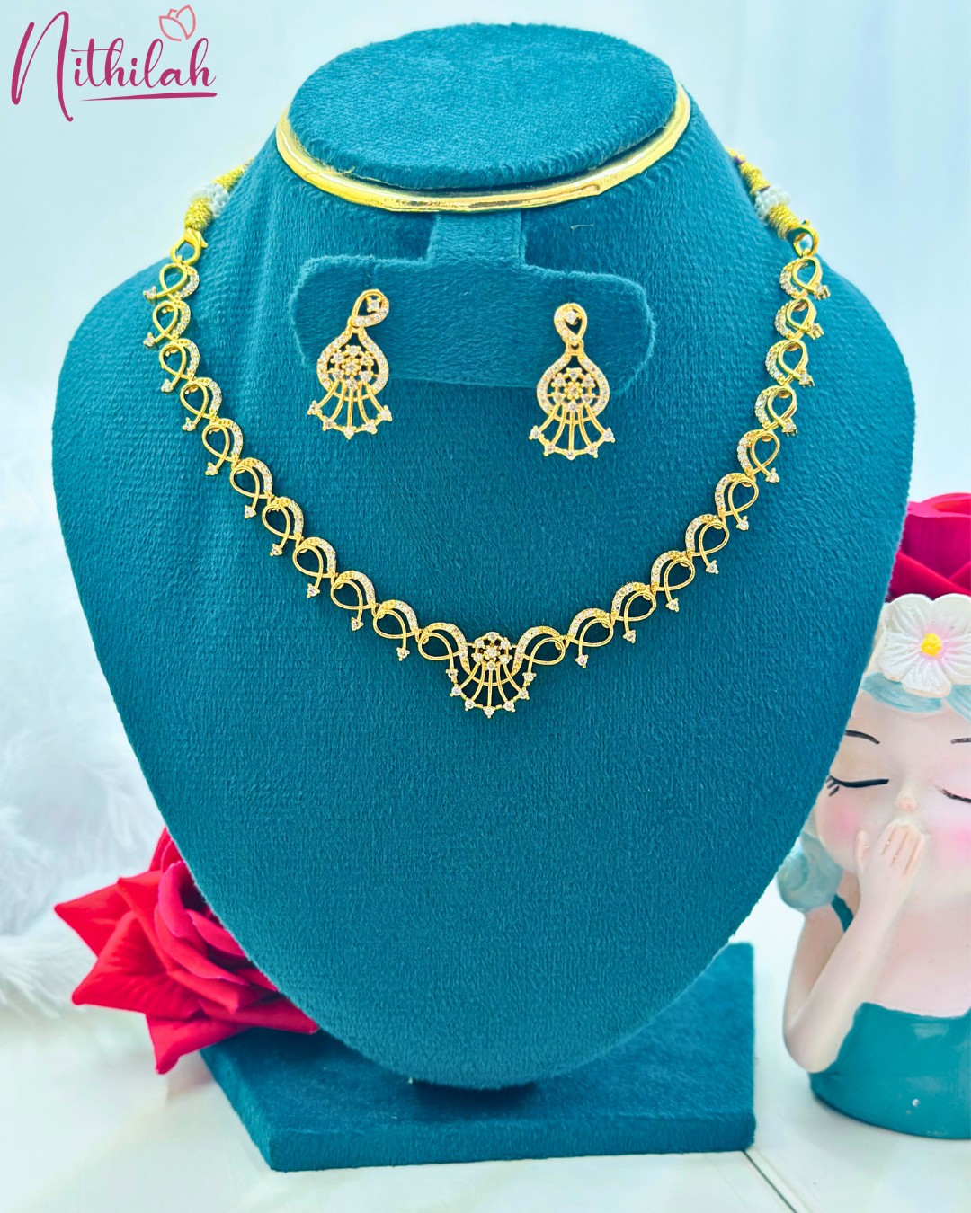 Gold-plated paisley CZ necklace with a fan-shaped centre detail and matching earrings on a teal display bust