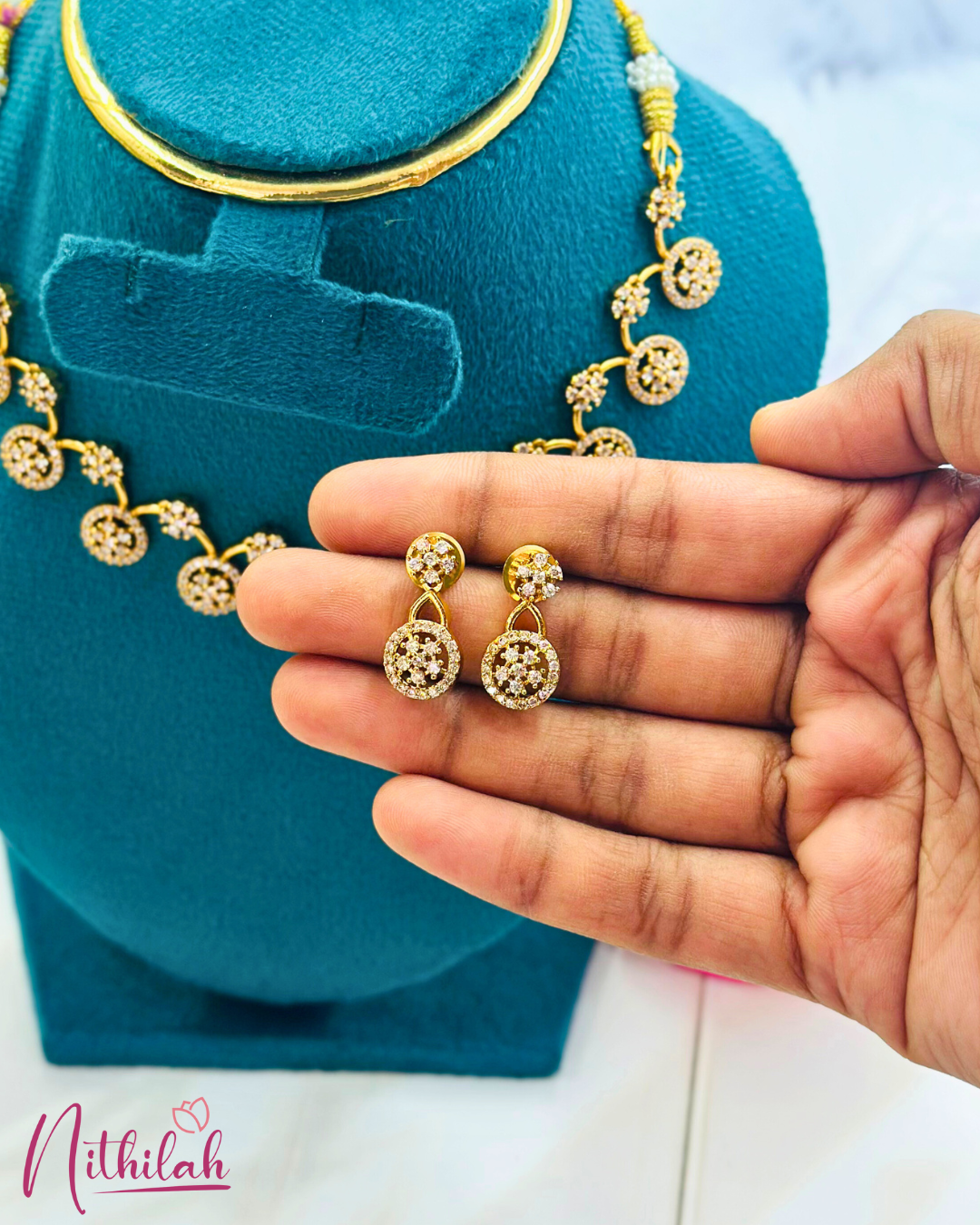 Close-up of gold-plated round CZ drop earrings with small floral studs, held in a hand