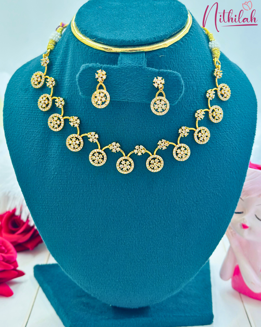 Gold-plated necklace with circular CZ motifs, floral clusters and matching round earrings on a teal display bust