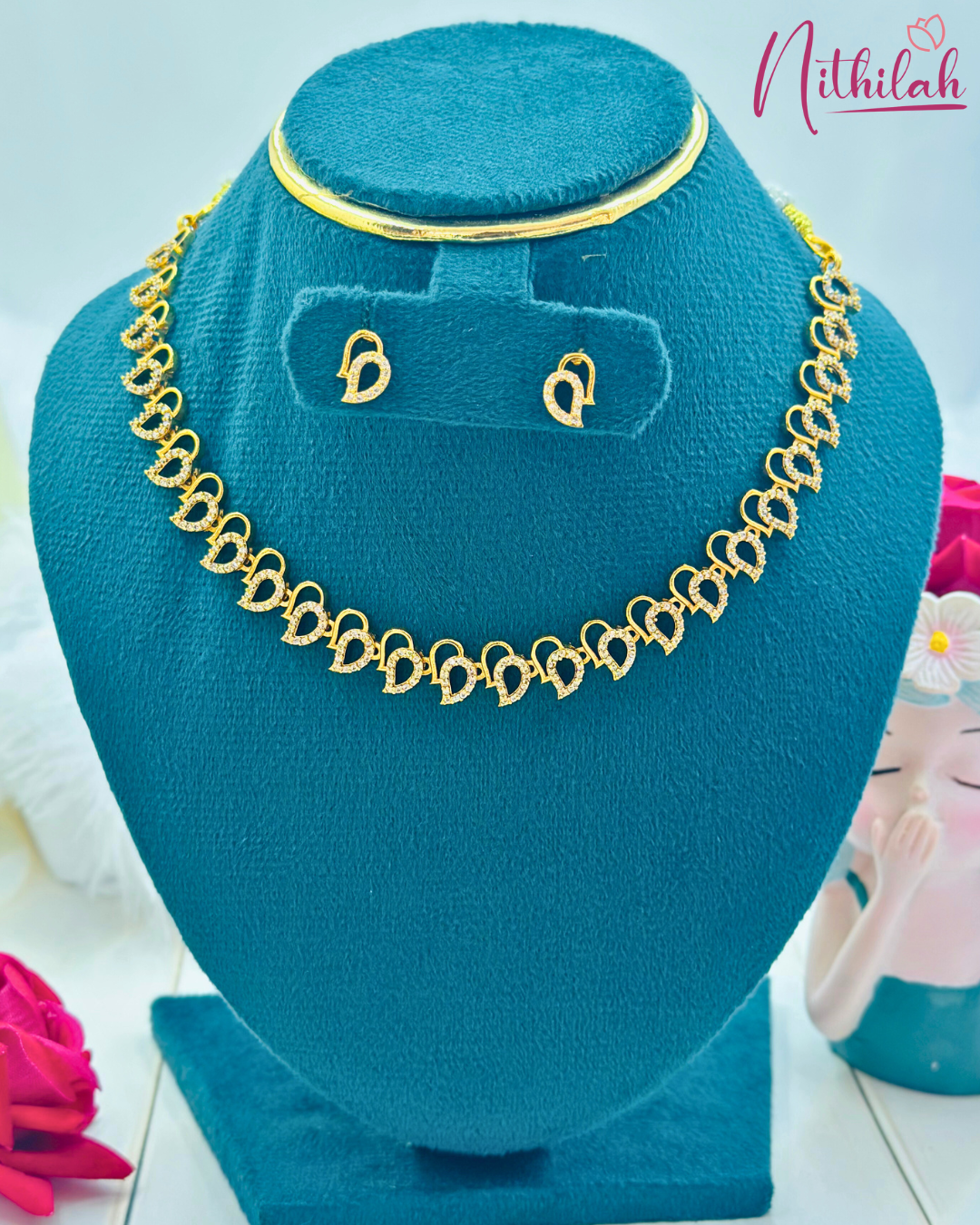 Gold-plated teardrop CZ necklace and matching stud earrings on a teal display bust