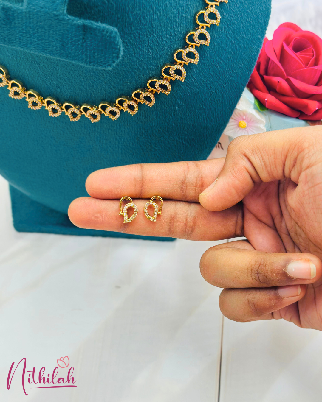 Close-up of gold-plated open teardrop stud earrings with CZ accents, held on fingertips