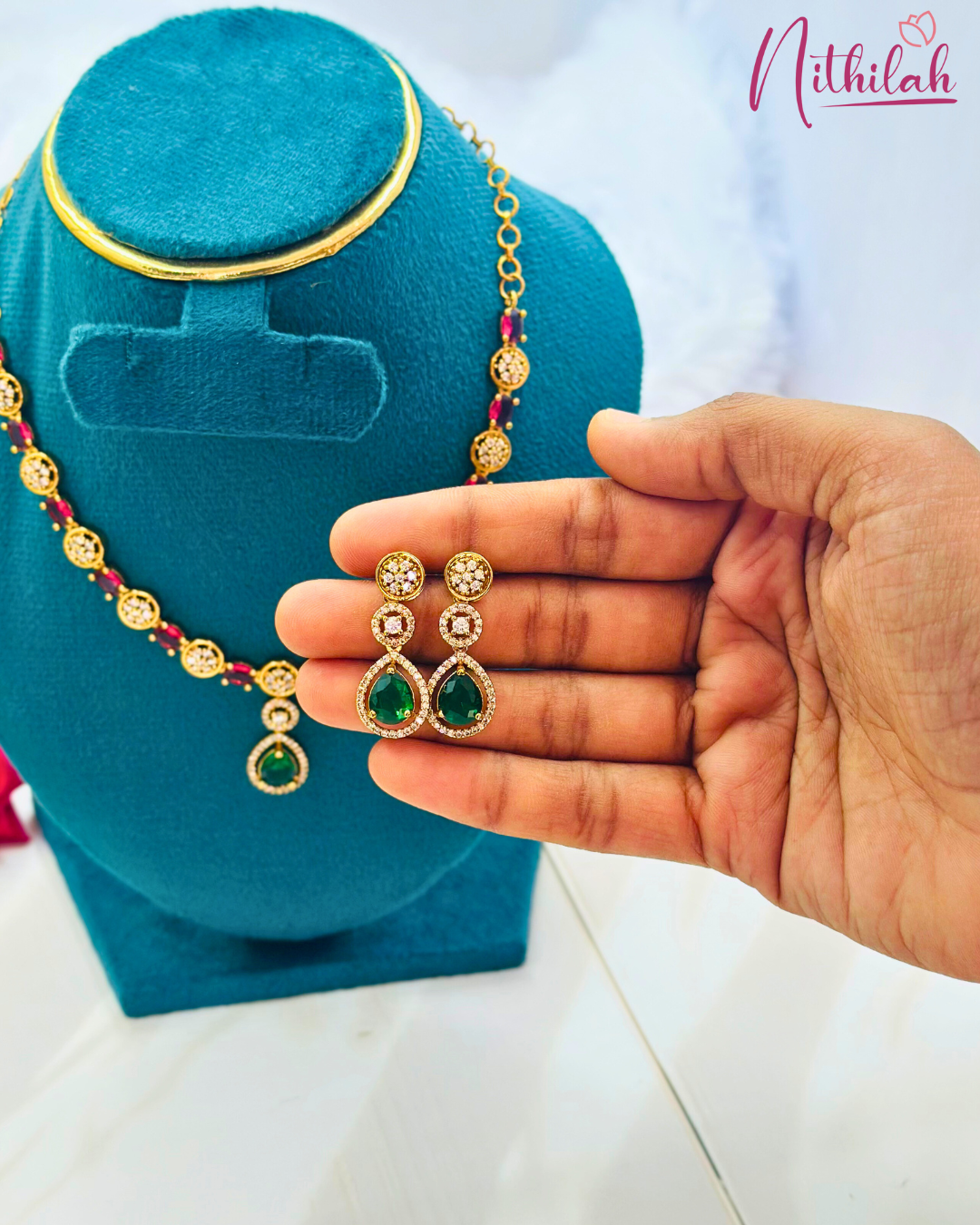 Close-up of matching gold-plated green teardrop CZ earrings held in a hand