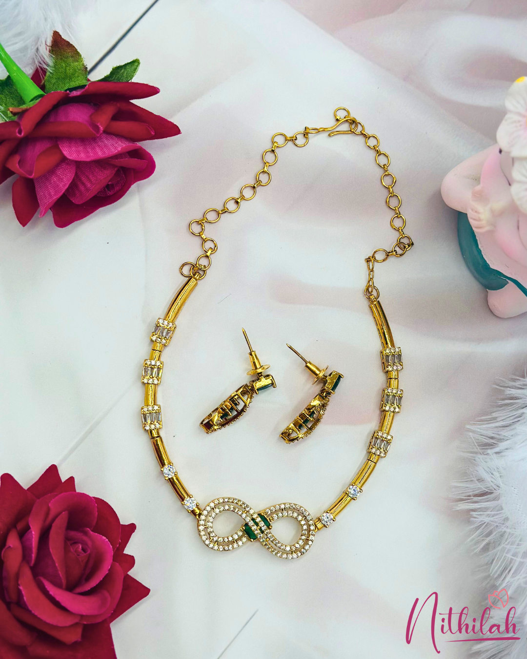 Gold-plated CZ infinity necklace set laid flat with matching earrings and adjustable extension chain