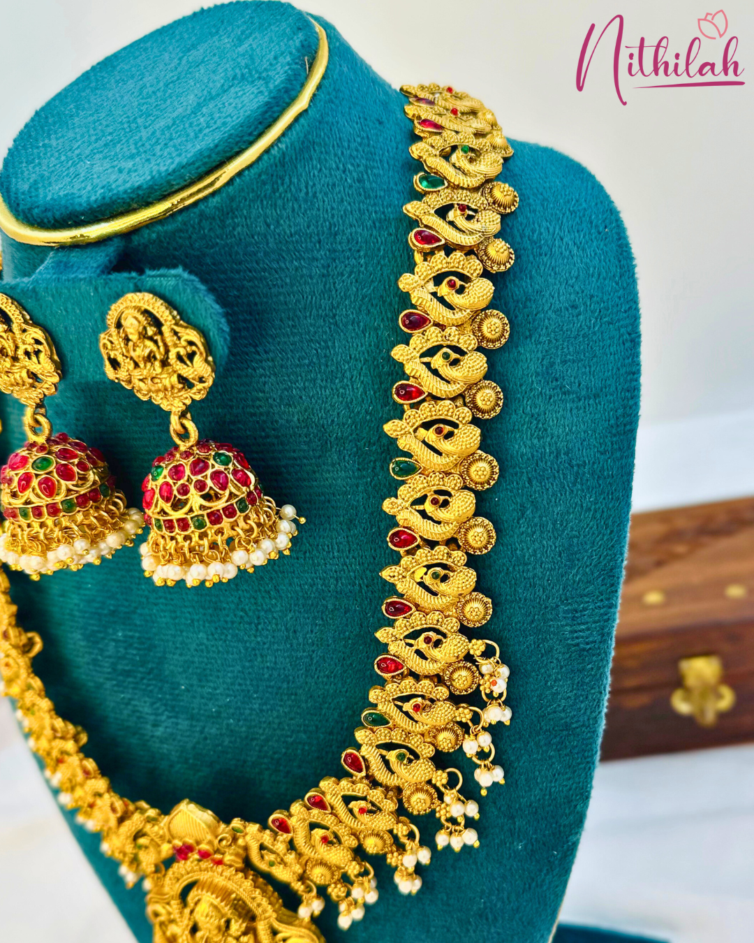 Angled close-up of the Lakshmi haaram showing textured peacock motifs, red and green accents and cream-coloured bead fringes