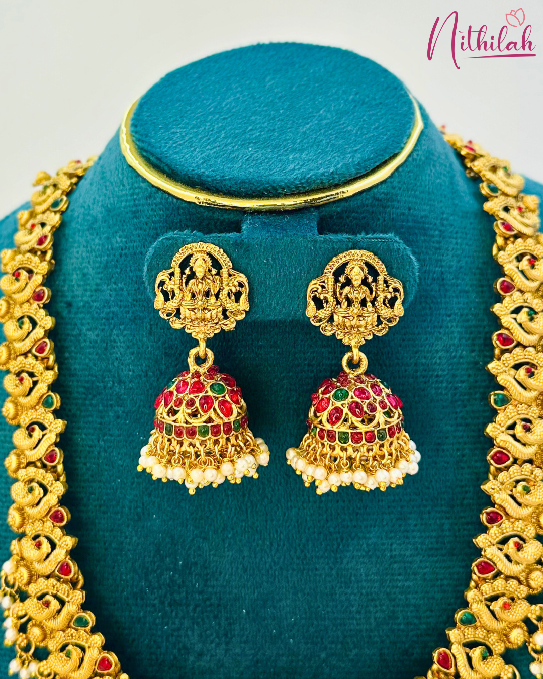 Close-up of matching jhumkas with Lakshmi-motif studs, red and green accents and cream-coloured bead drops