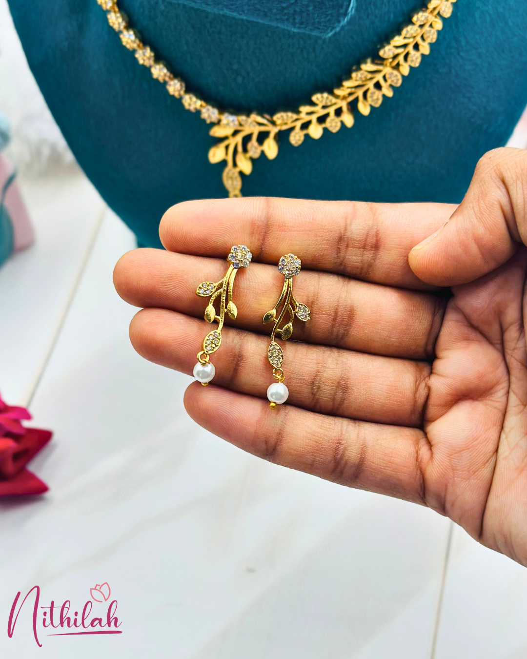 Close-up of gold-finish leaf CZ earrings with white pearl drops, held in a hand