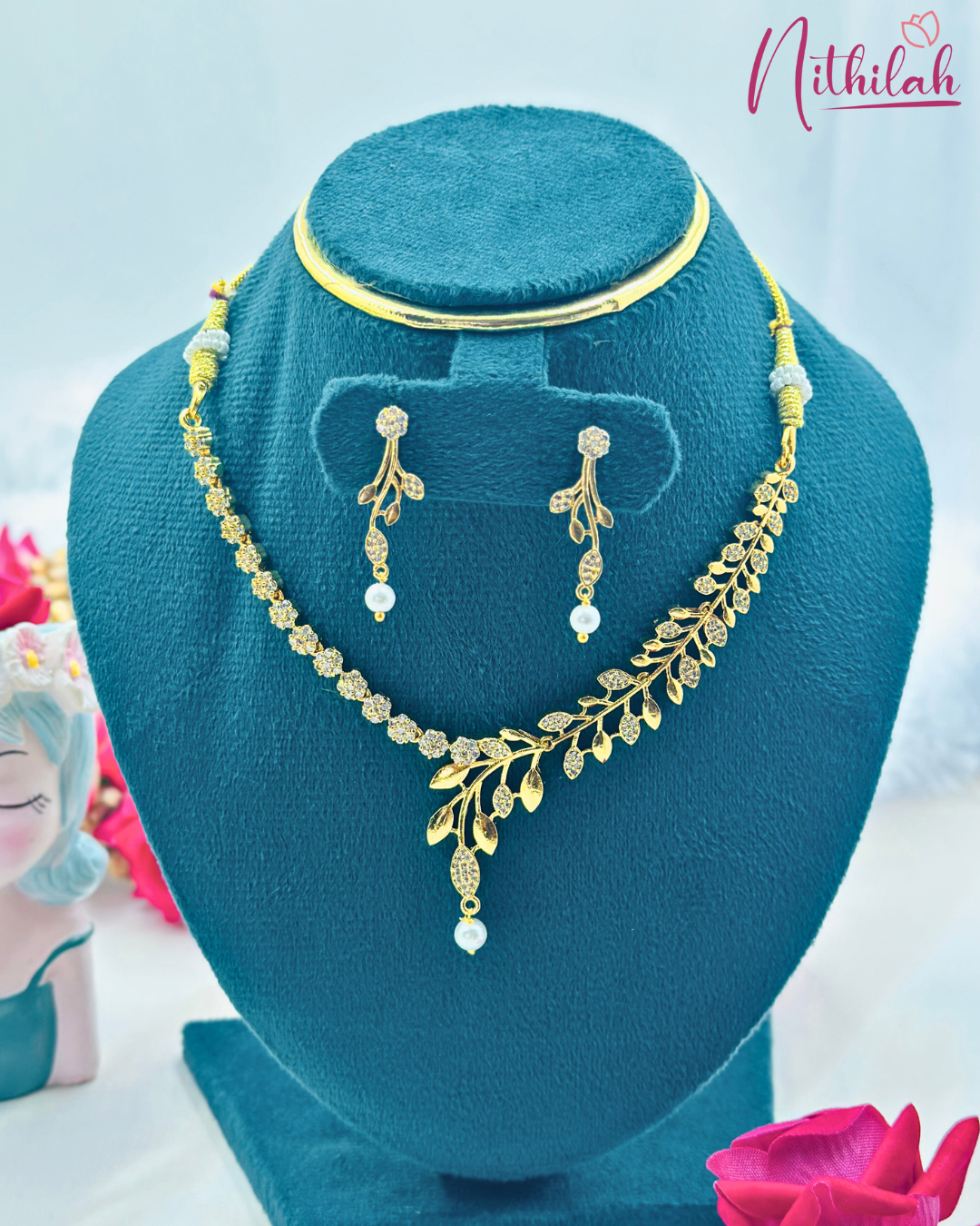 Gold-finish leaf CZ necklace set with pearl drops and matching earrings on a teal display bust