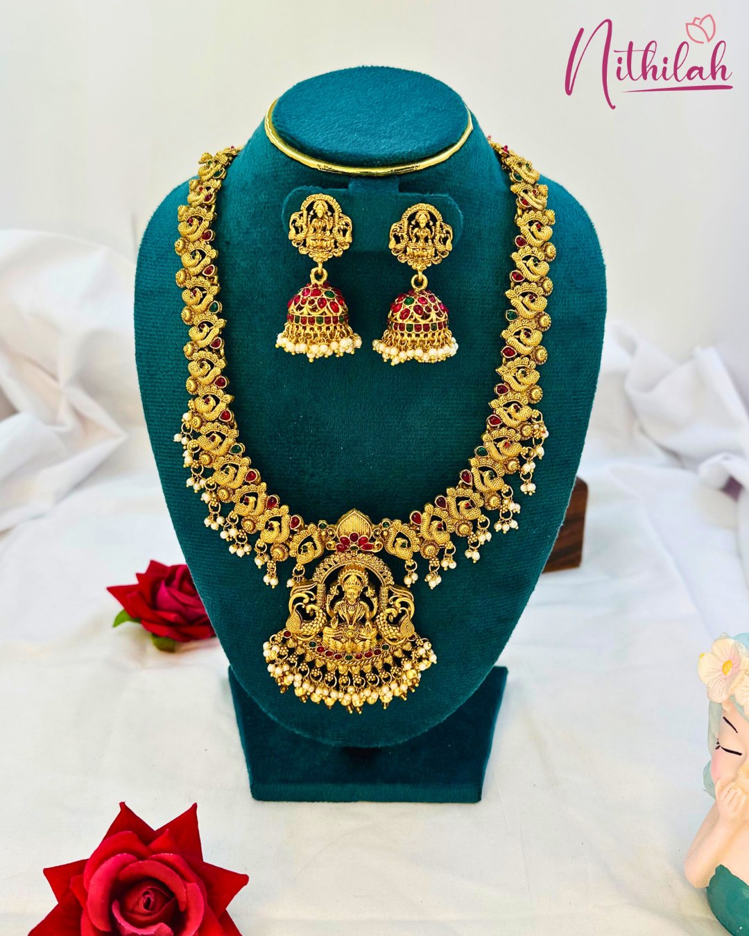 Matte gold-tone Lakshmi haaram with peacock motifs, cream-coloured bead fringes and matching jhumkas on a teal display bust