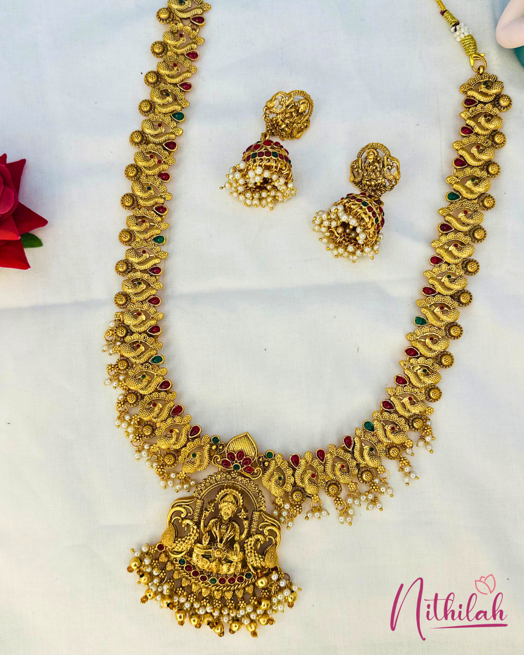 Lakshmi haaram and matching jhumkas laid flat, showing the large pendant, peacock motifs and cream-coloured bead detailing