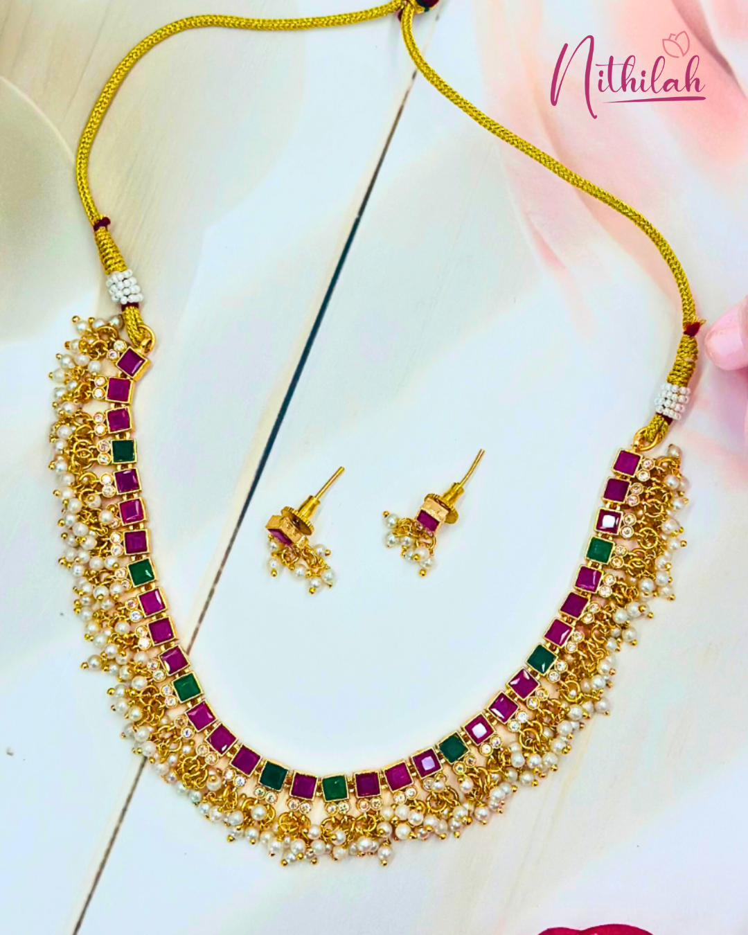 Gold-plated necklace set with square ruby-pink and green stones, pearl-drop fringe and matching earrings laid flat