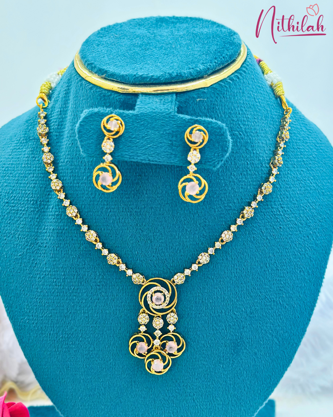 Gold-finish pink swirl pendant necklace with three hanging drops and matching earrings on a blue jewellery stand