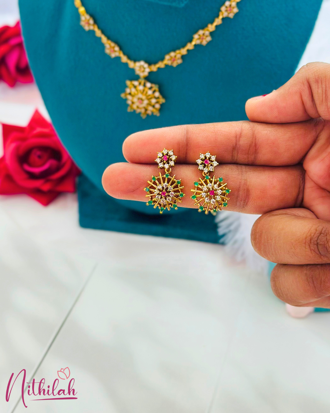 Close-up of gold-finish starburst drop earrings with ruby-coloured centres, green accents and clear stones