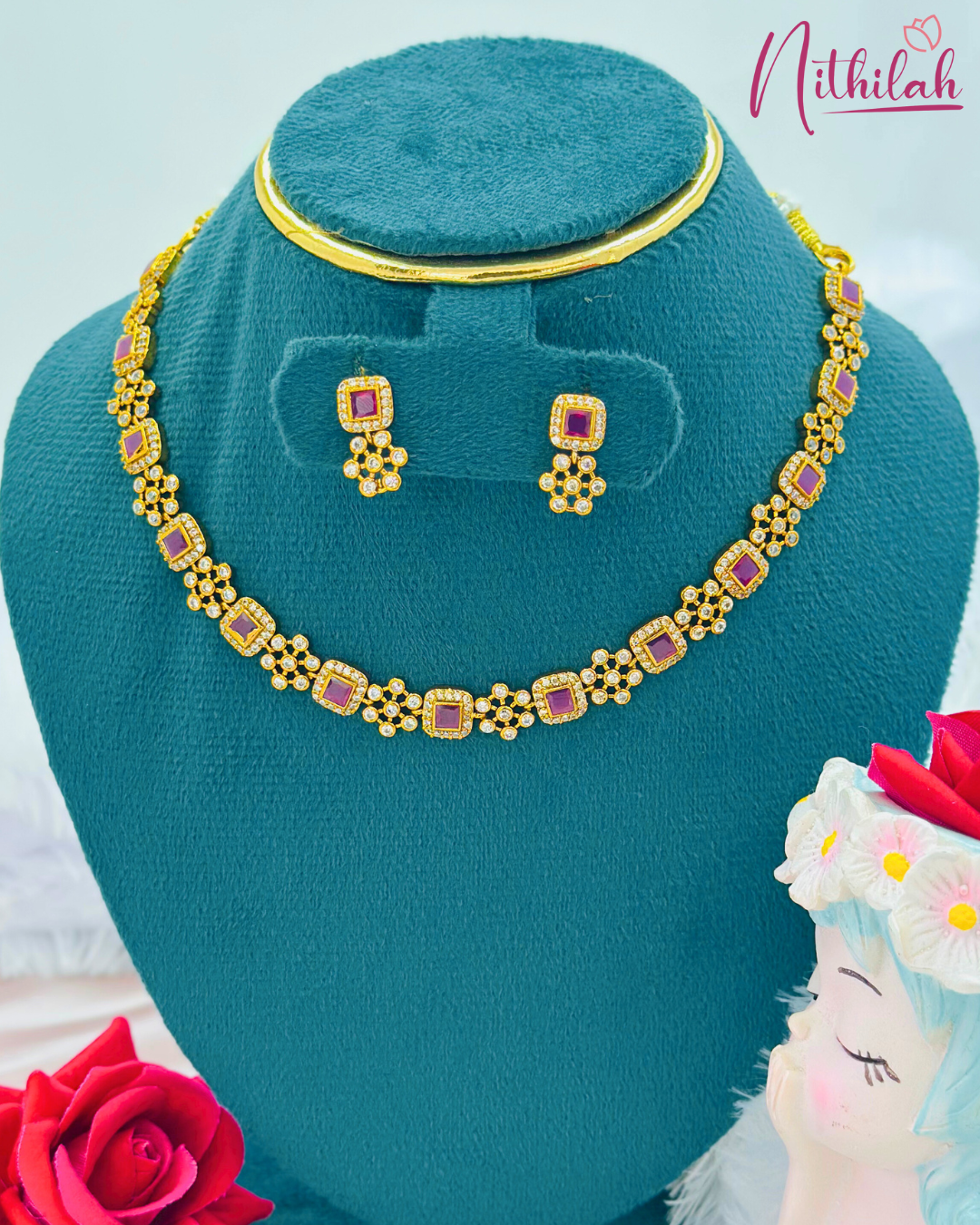 Ruby-pink square stone AD necklace and matching earrings displayed on a blue jewellery stand