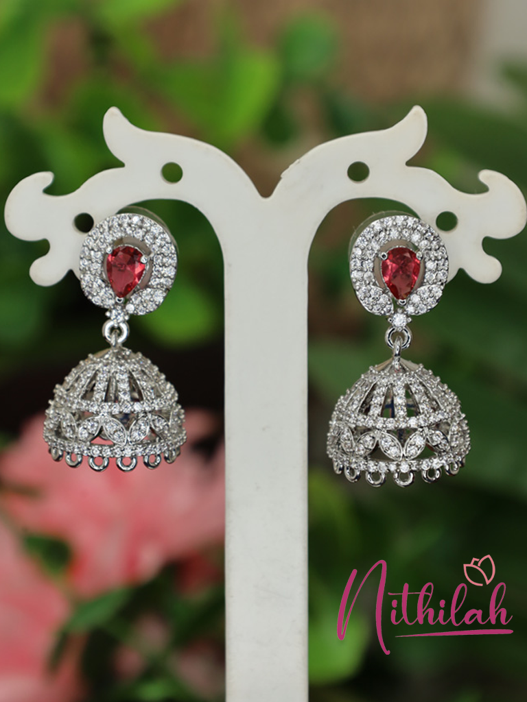 Pair of silver-tone American Diamond jhumka earrings with red teardrop centre stones and sparkling dome-shaped drops displayed on a jewellery stand.