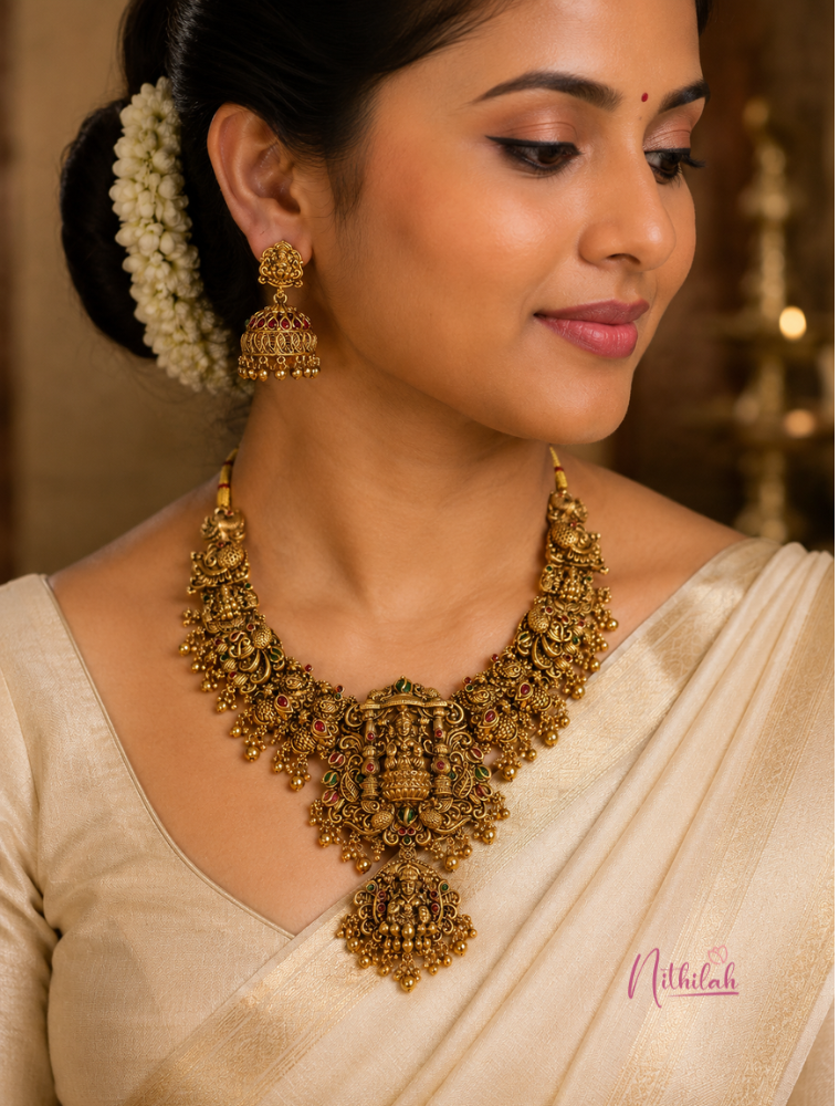 South Indian model wearing Antique Lakshmi Temple Jewellery Necklace Set with matching jhumka earrings featuring Goddess Lakshmi, peacock motifs and traditional red and green Kemp stones.