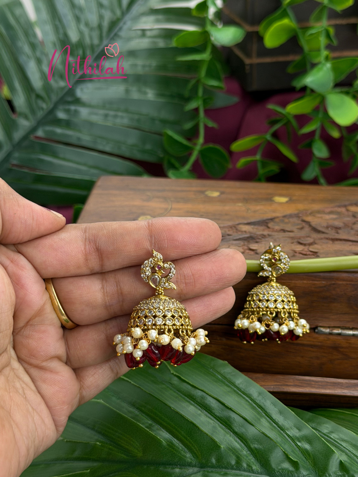 Traditional CZ jhumka earrings with red beads and pearl drops shown in hand