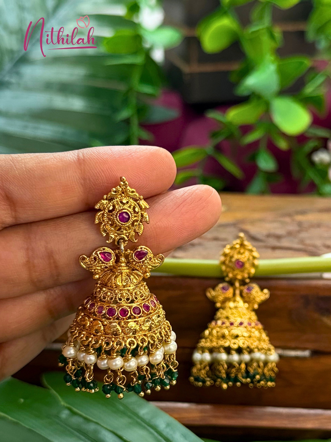Traditional gold tone jhumka earrings with pearl and bead drops shown in hand
