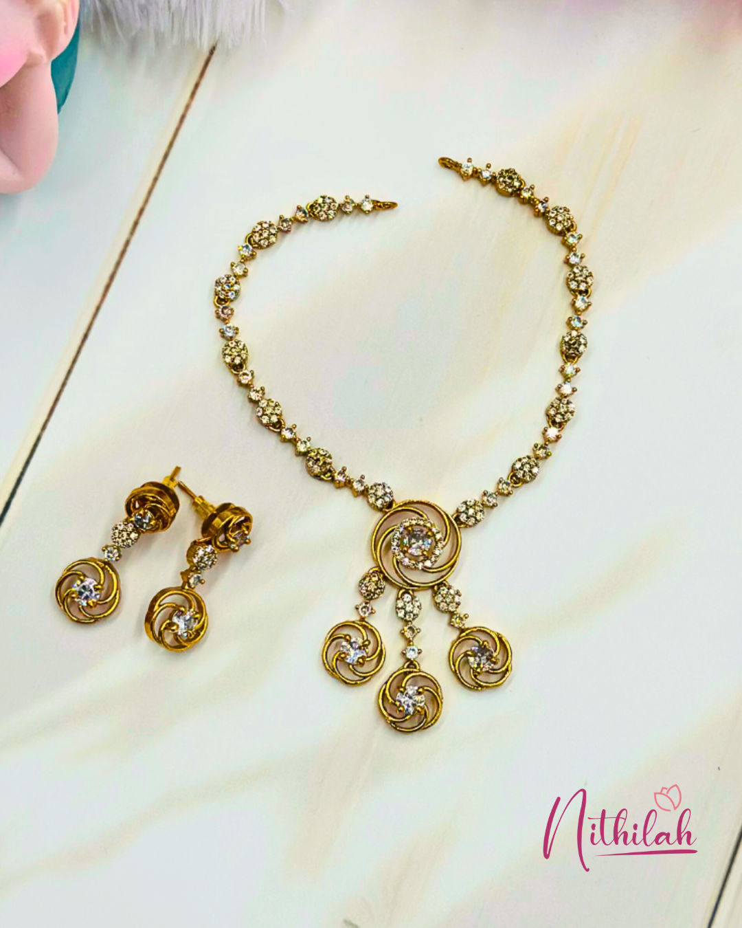 Detailed flat lay of the white AD necklace set, showing its swirl pendant, three circular drops and matching earrings