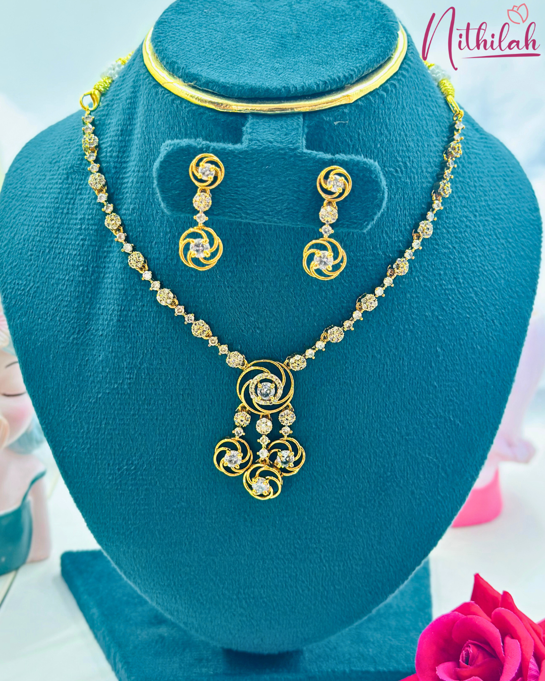 White AD swirl pendant necklace with three dangling circular drops and matching earrings on a blue jewellery stand